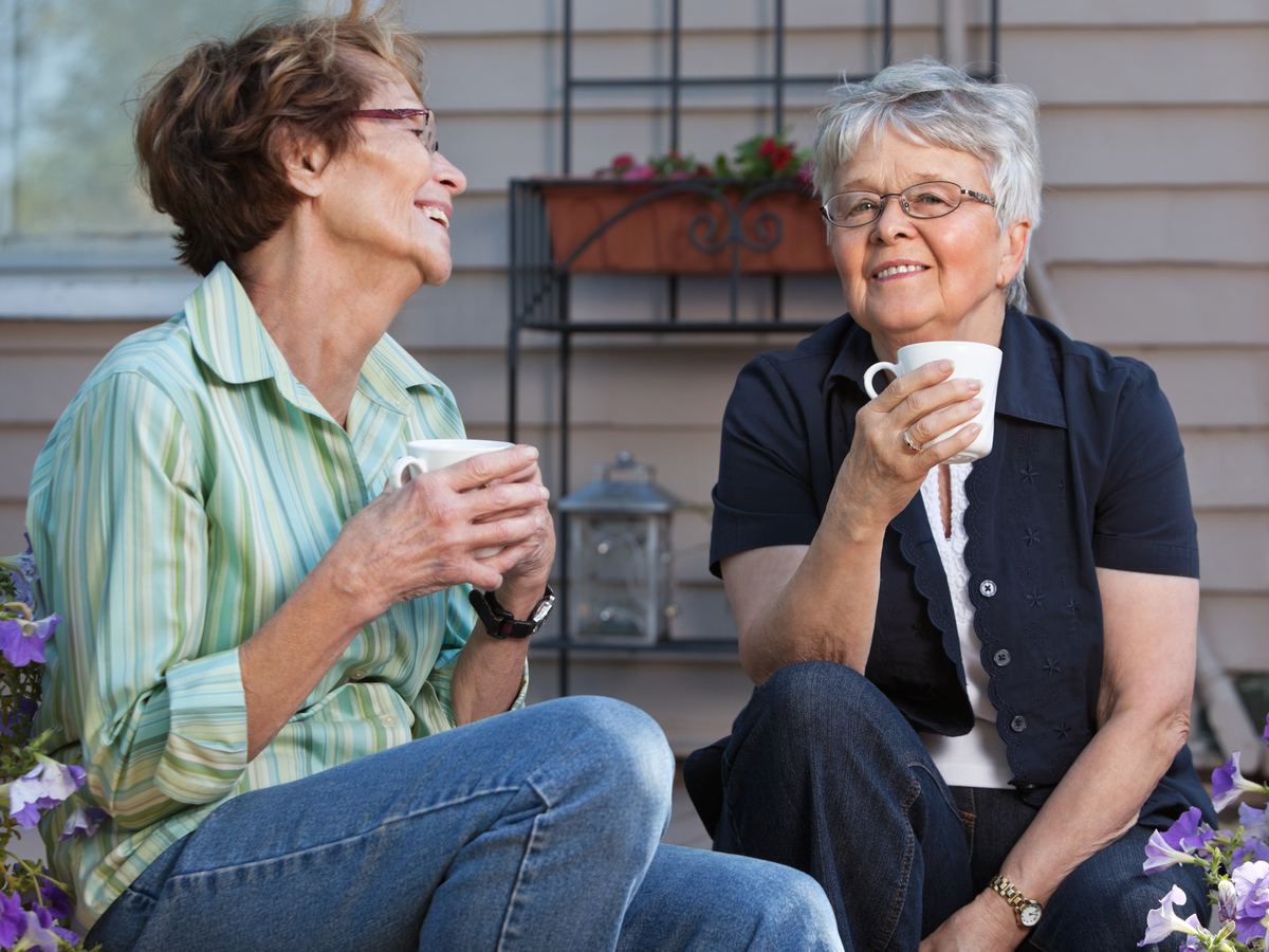 Two older women laughing over coffee on a patio